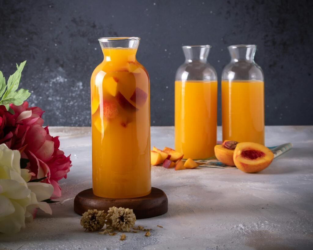 Refreshing peach juice in glass bottles with fresh peaches and flowers on a rustic table.