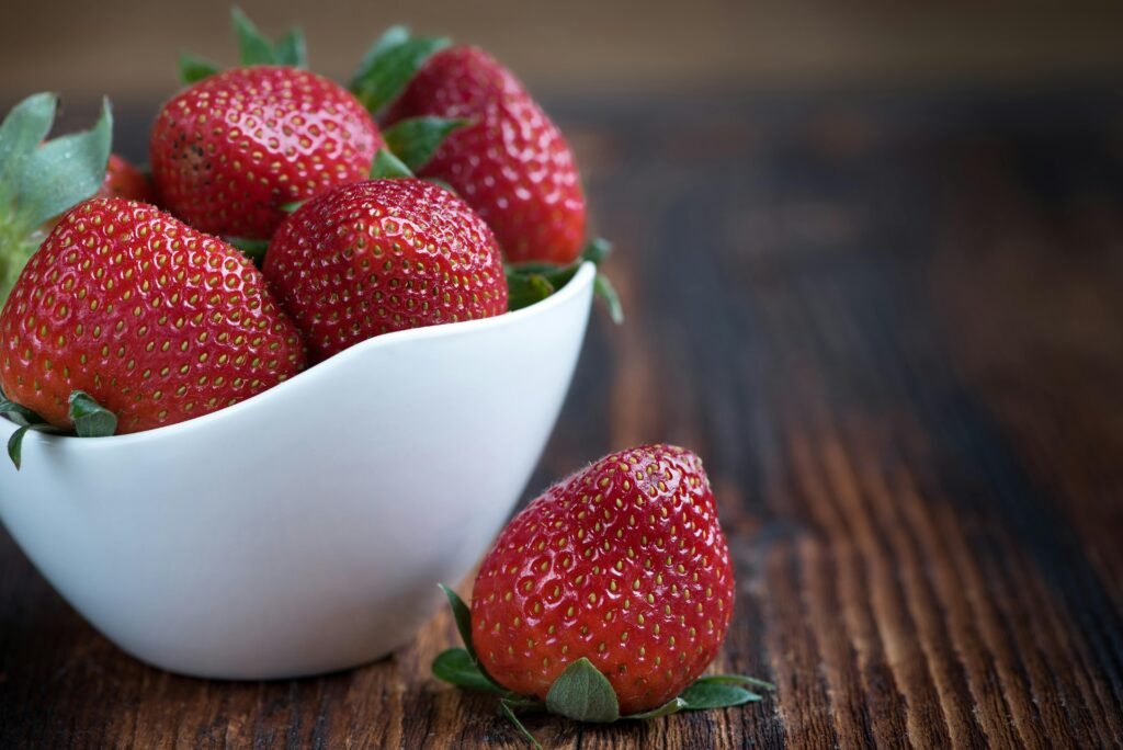 Close-up of fresh strawberries in a white bowl on a rustic wooden table, highlighting vibrant red color.